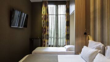 Une chambre d’hôtel avec deux lits, un téléviseur à écran plat fixé au mur, un radiateur et une fenêtre avec des rideaux.