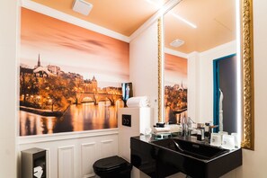A bathroom with a large mirror, a sink, and a toilet. There is a painting of a cityscape on the wall.
