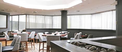 Un salón de conferencias moderno con techo alto, ventanas amplias y una mesa central con sillas.