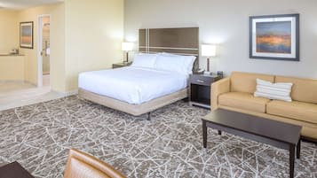 A hotel room with a bed, bedside tables, a sofa, a coffee table, and a patterned carpet.