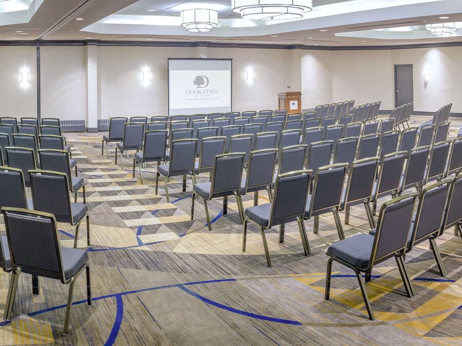 Een congreszaal met rijen stoelen, een spreekgestoelte en een presentatiescherm.