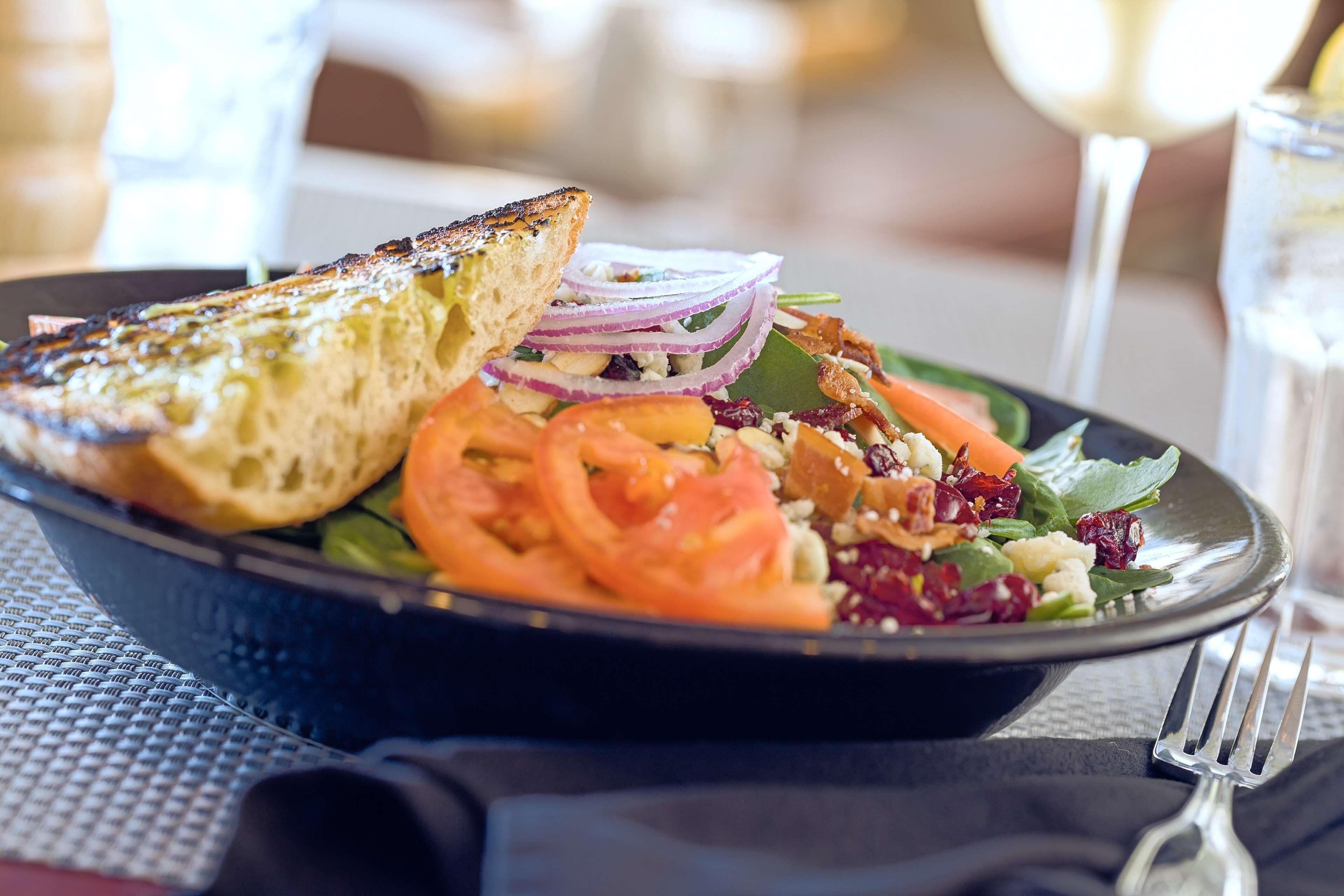 Une assiette de nourriture comprenant une tranche de pain grillé, des tomates, des oignons et des légumes verts.