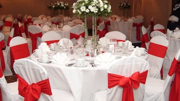A banquet hall with round tables set for a formal event, each with white tablecloths and red sashes on the chairs.