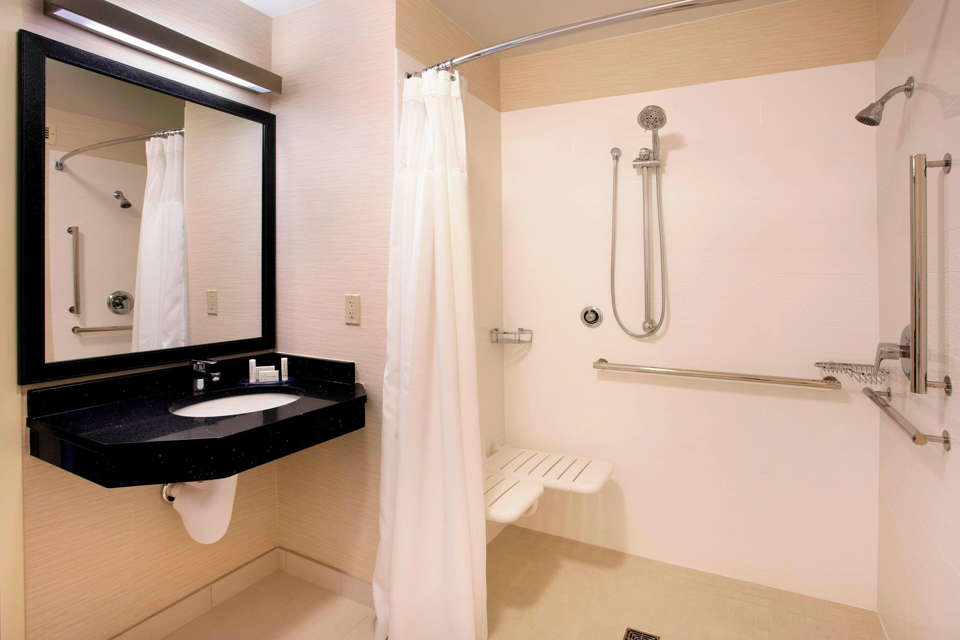 Une salle de bain moderne avec un lavabo noir, un miroir, une douche équipée d’un pommeau de douche amovible et d’une barre d’appui.