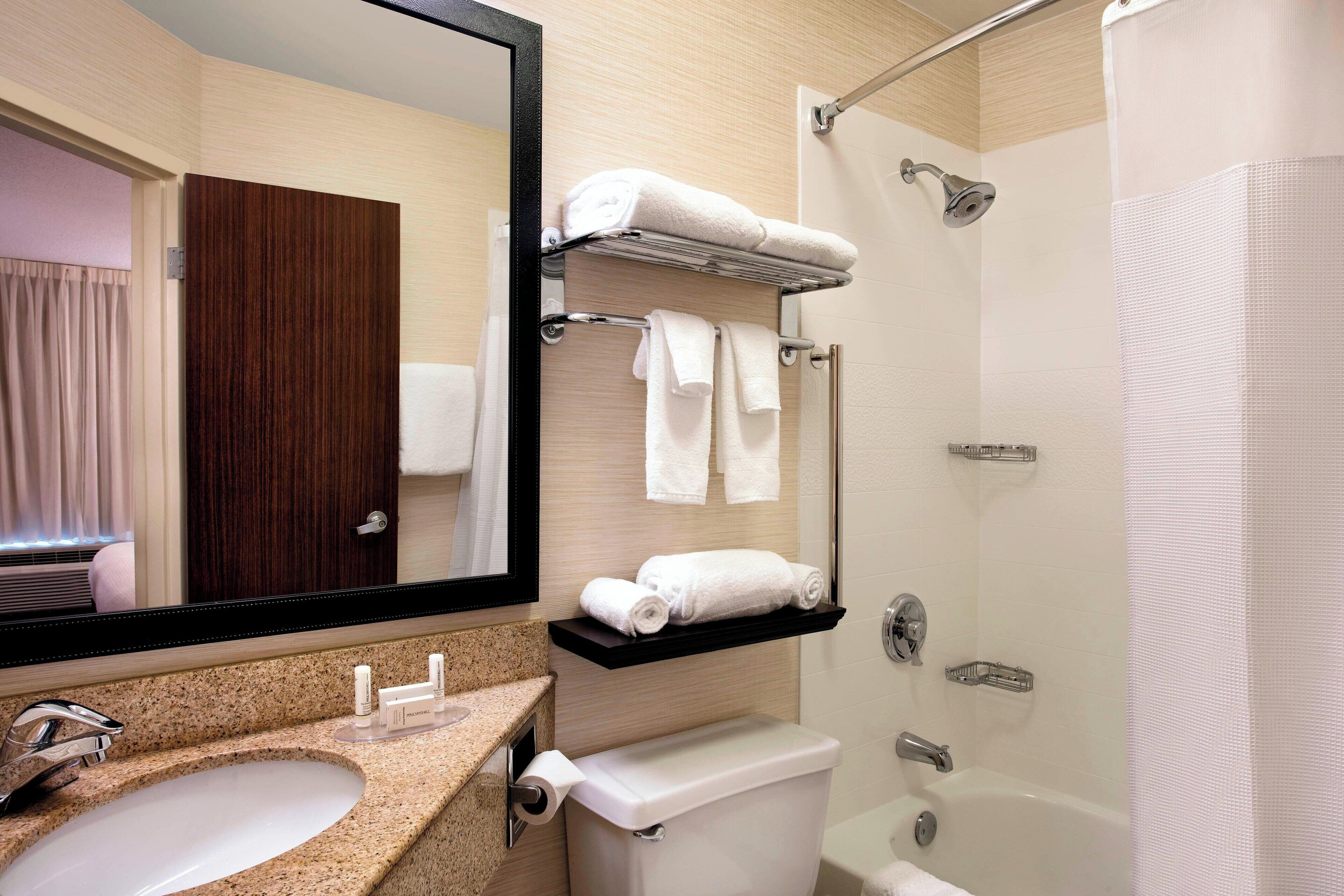 A modern bathroom with a granite sink, a toilet, a shower with a glass door, and a mirror with a wooden door.