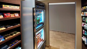 Habitación de hotel con minibar, refrigerador con dispensador de bebidas y estantes llenos de aperitivos y refrescos.