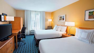 A hotel room with two beds, a desk with a TV, a chair, a desk lamp, and a window with curtains.