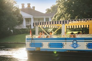 A boat with passengers, a house in the background, and a flag.