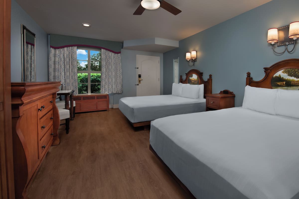 Habitación de hotel con dos camas, tocador, cómoda y ventana con cortinas.