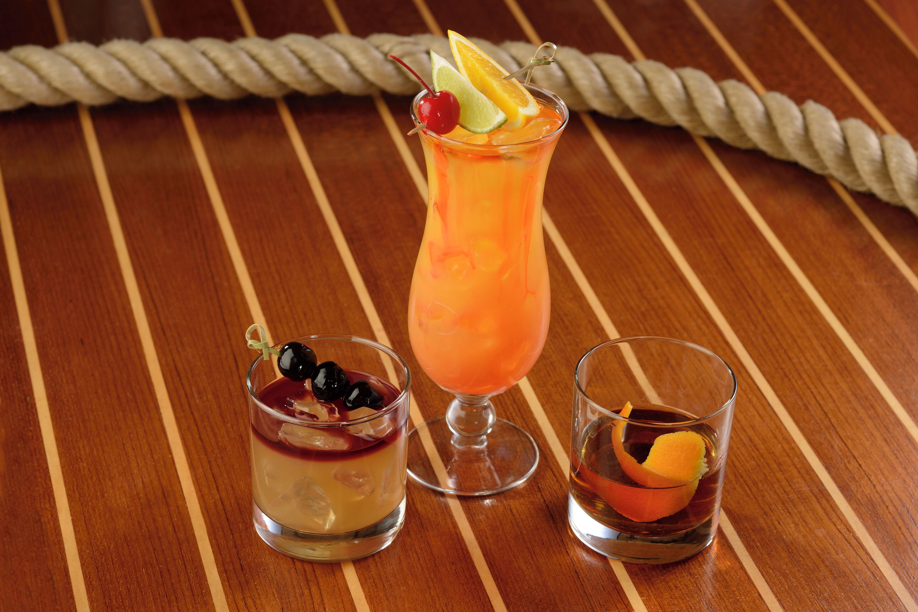 Three drinks on a wooden table with a rope in the background.