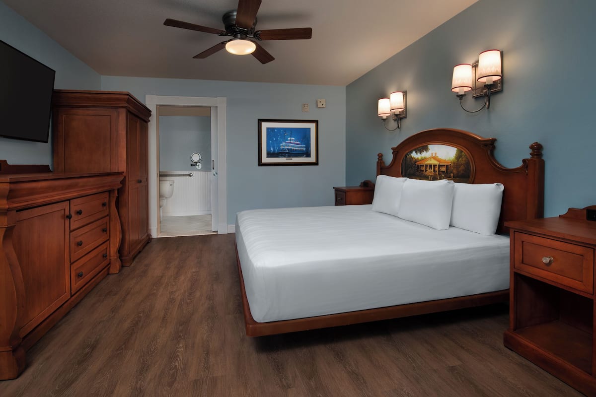 Habitación de hotel con una cama grande, muebles de madera, ventilador de techo e iluminación empotrada.