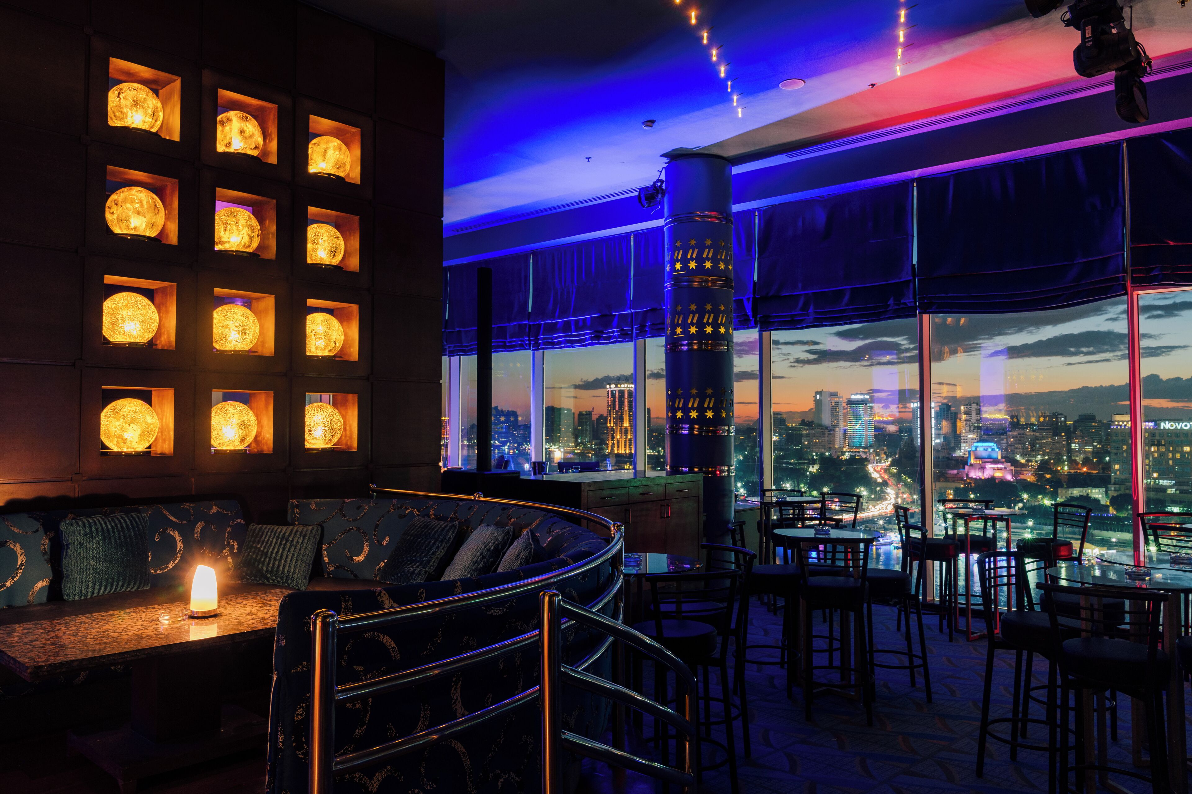 A rooftop bar with a city view, illuminated by string lights and featuring a seating area with a candle.