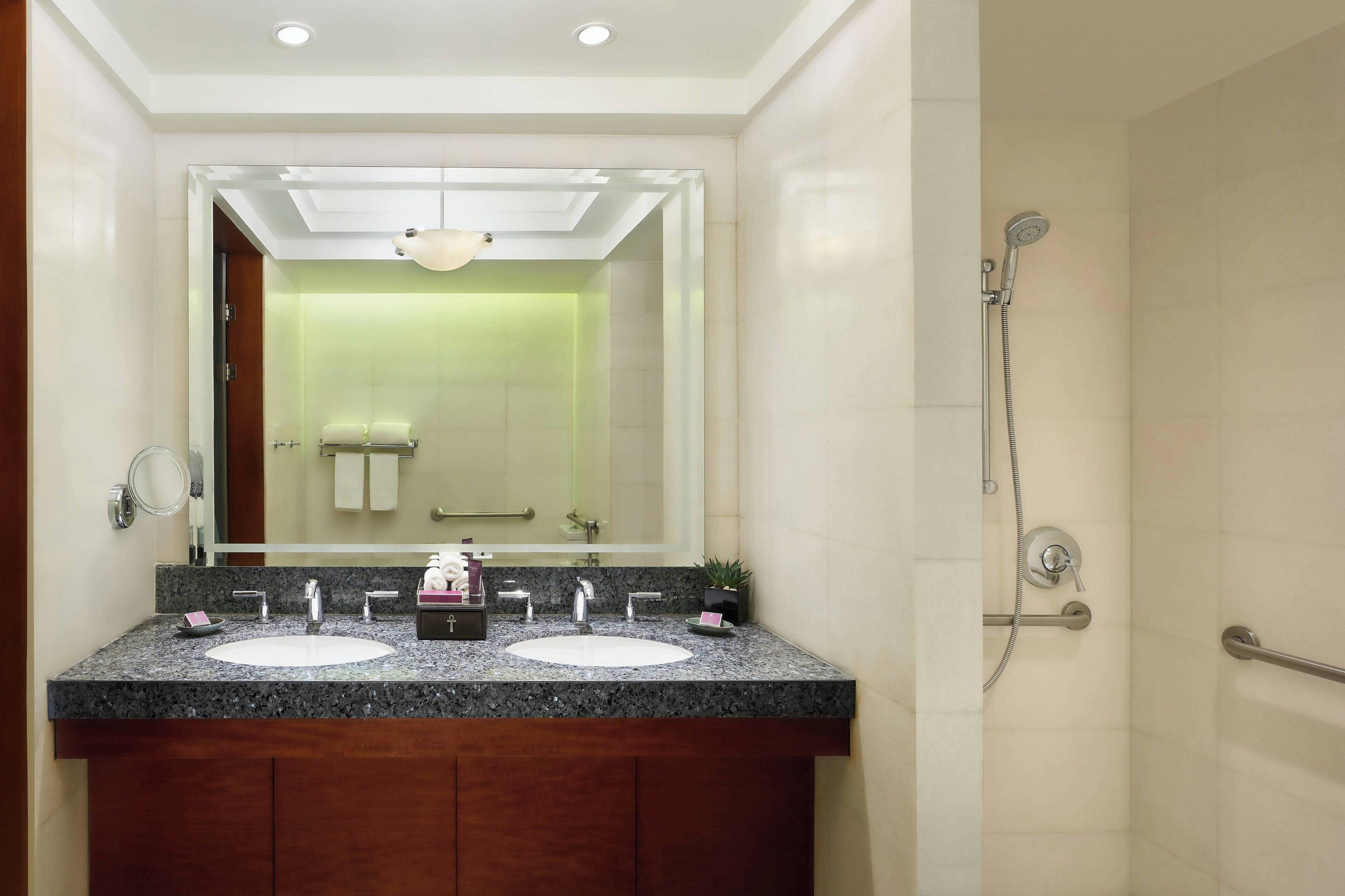 A bathroom with two sinks, a large mirror, a shower, and a handrail.