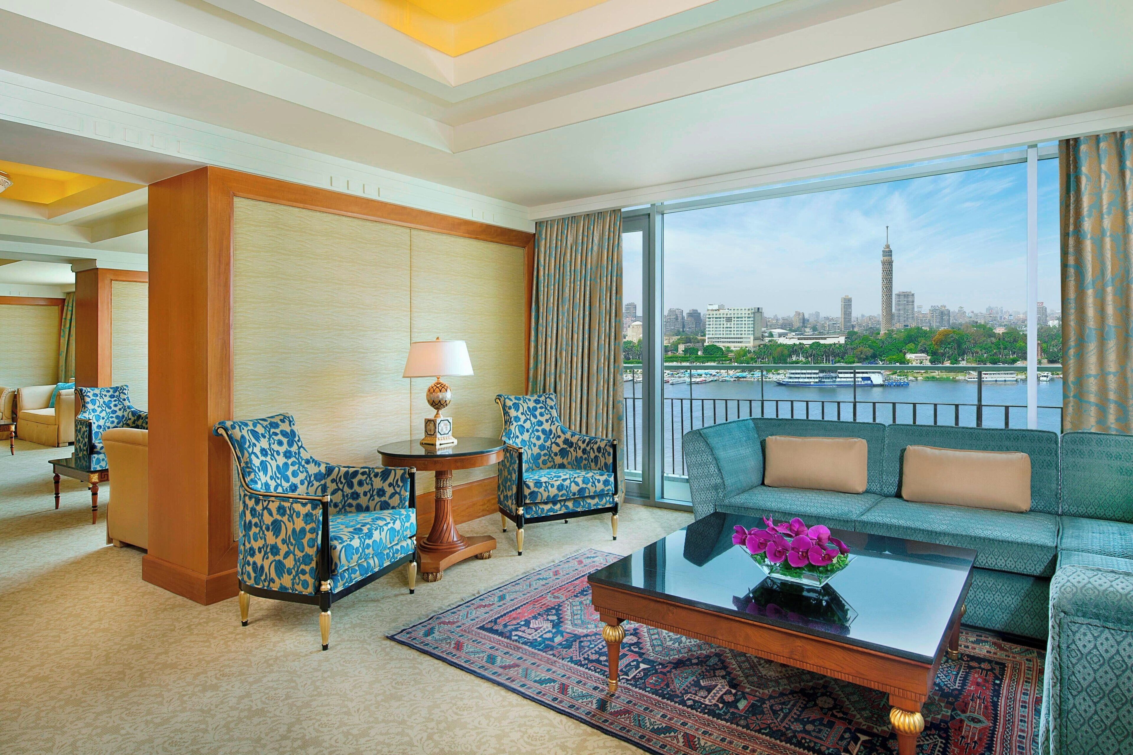 A hotel room with a sofa, two armchairs, a coffee table, and a view of a city skyline.