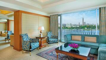 Habitación de hotel con sofá, dos sillones, una mesa de centro y vista a un horizonte urbano.