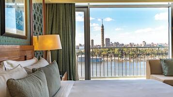 A hotel room with a large bed, a view of a cityscape, and a balcony with a railing.