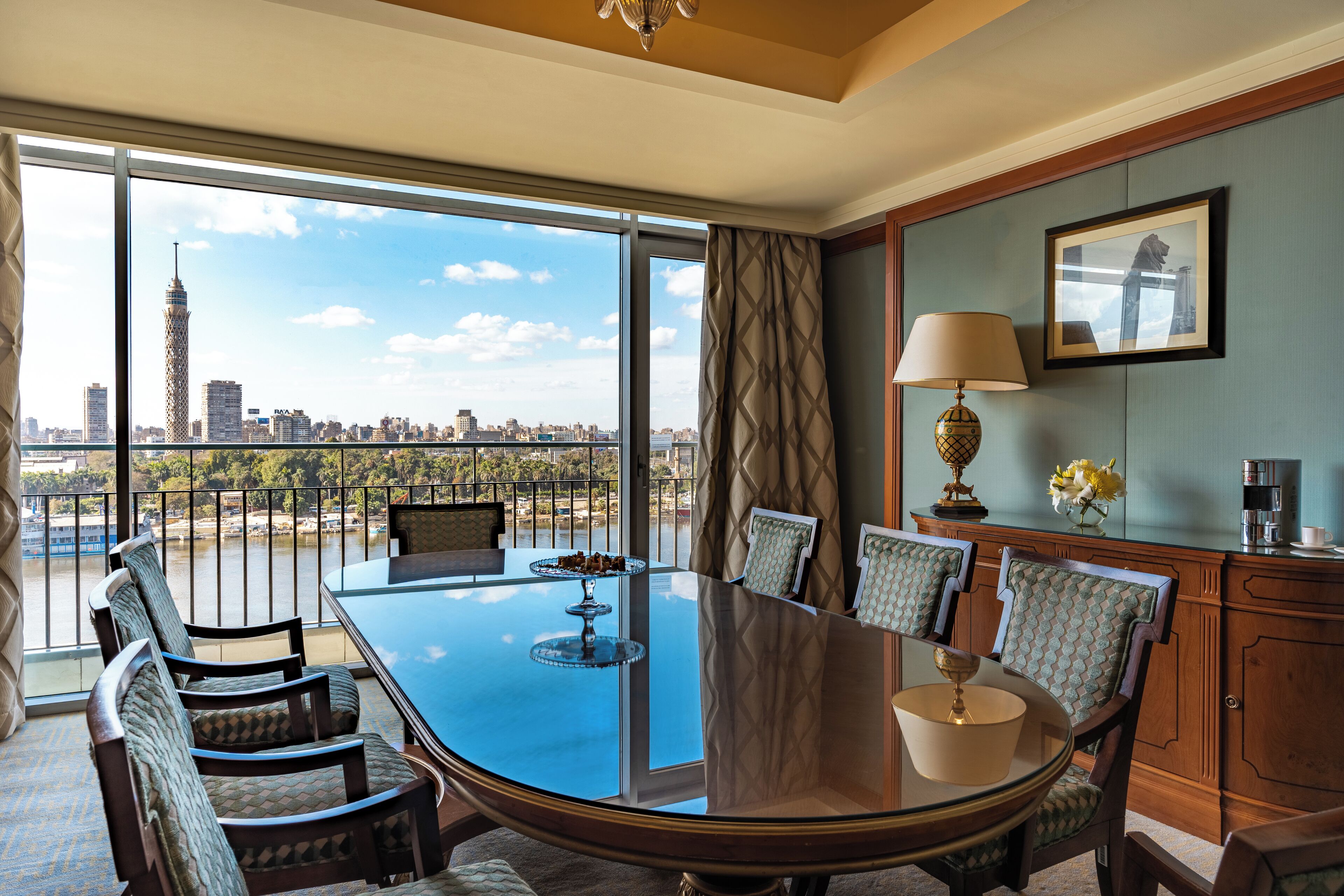 A conference room with a large glass table, chairs, a coffee machine, and a view of a city skyline.