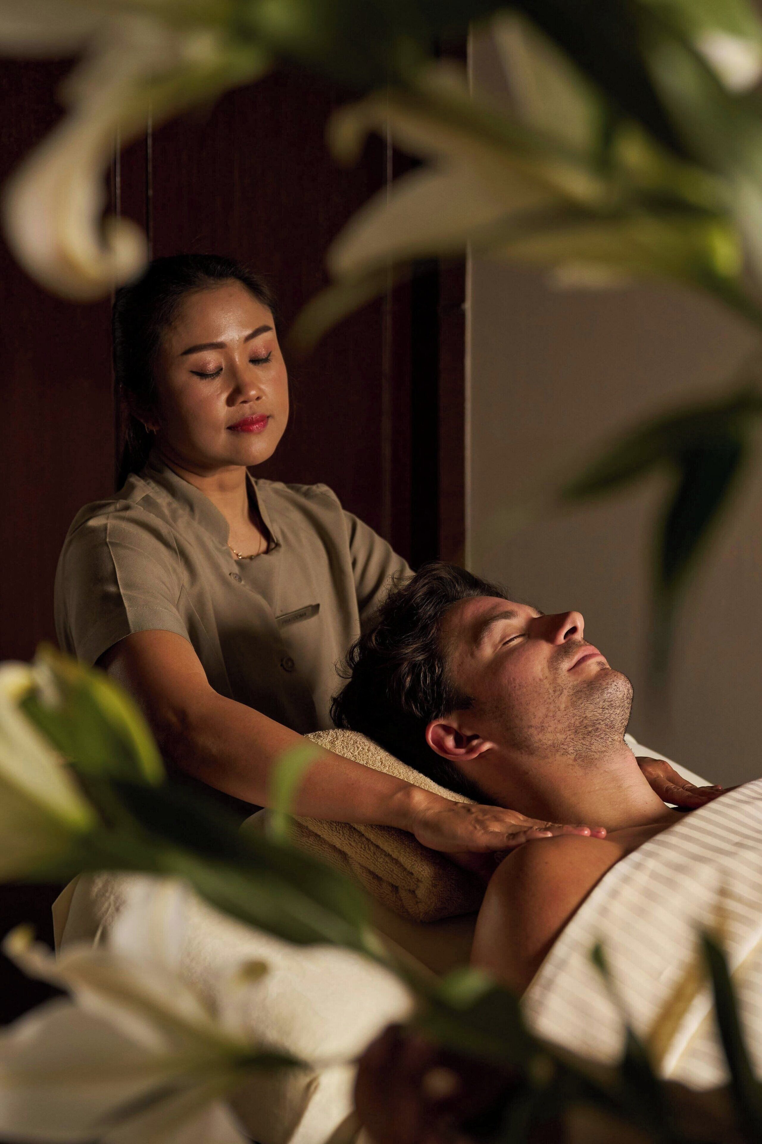 A person receiving a massage in a room with a wooden door and a plant in the foreground.