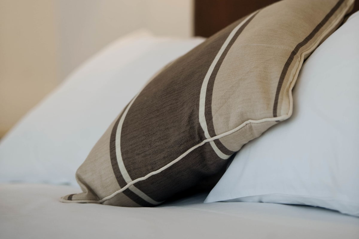 A bed with a pillow and a wall-mounted lamp.