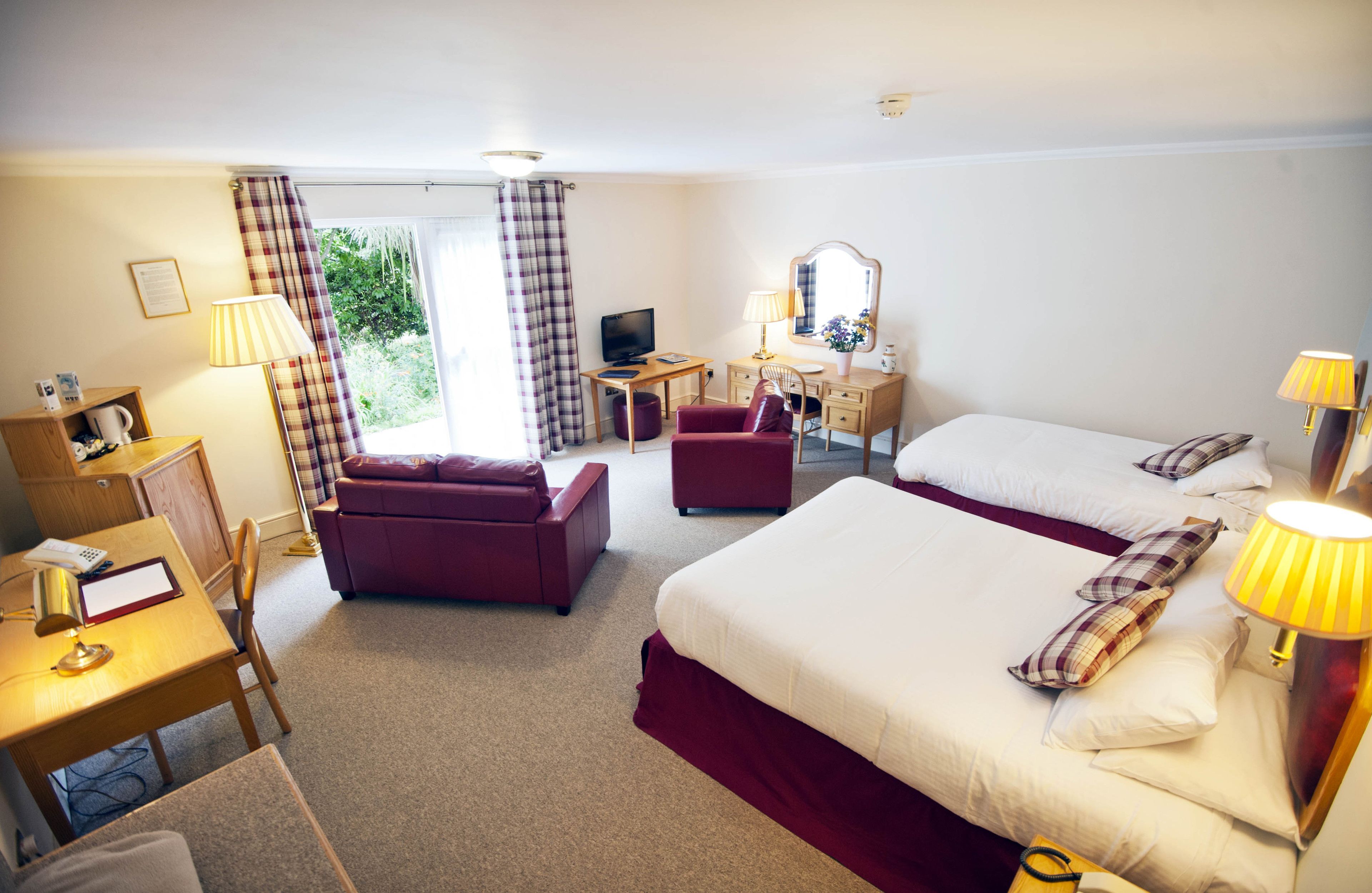 Ein Hotelzimmer mit zwei Betten, einem Schreibtisch mit Computer, einem Stuhl, einem kleinen Tisch und einem Fernseher.