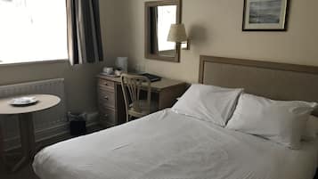 Ein Hotelzimmer mit einem Bett, einem Schreibtisch, einem Stuhl, einer Lampe, einem Spiegel und einem Bild an der Wand.