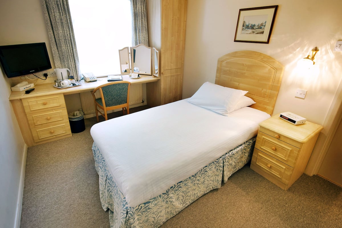 A hotel room with a bed, a desk, a chair, a TV, a bedside table with a lamp, and a picture on the wall.