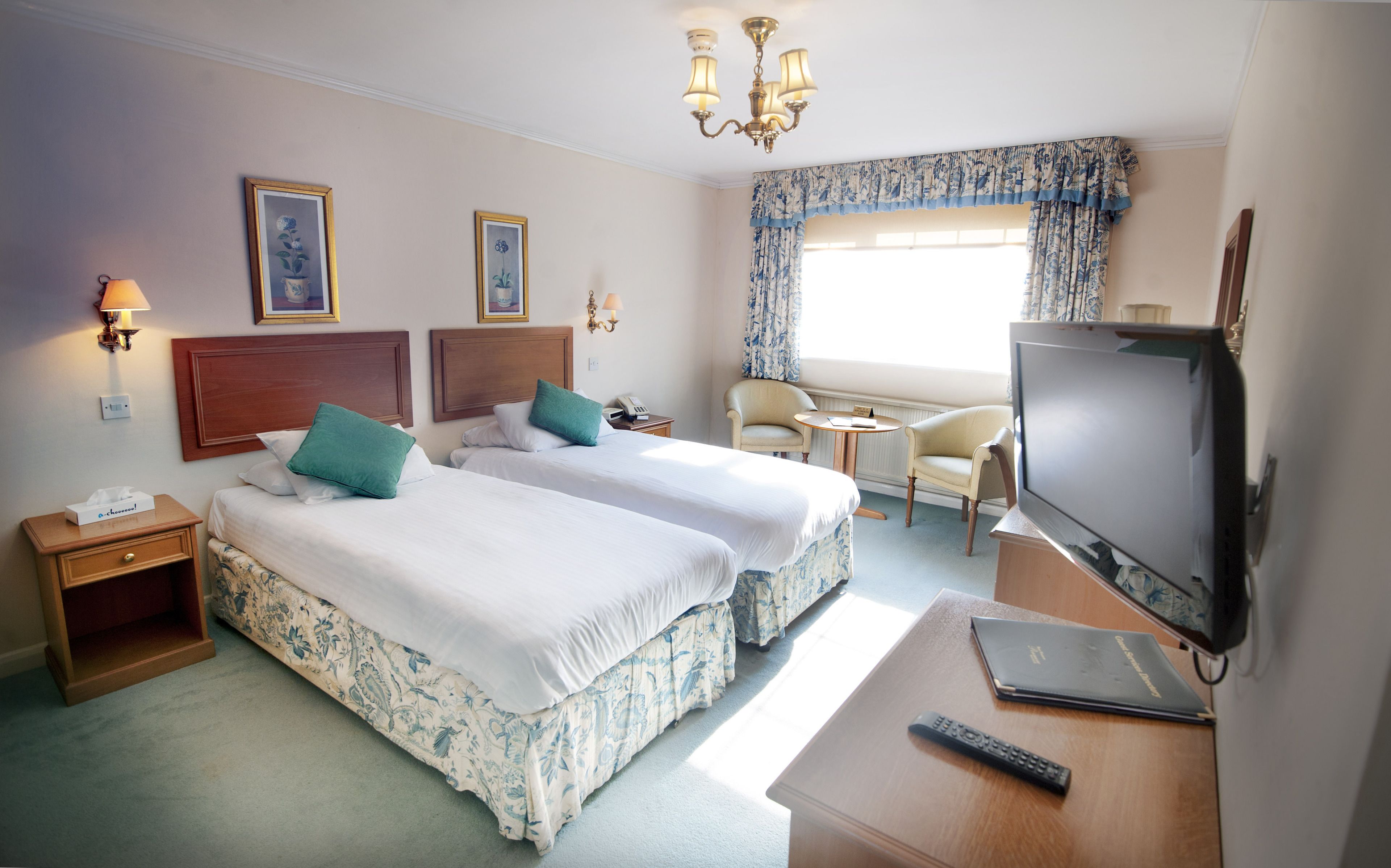 A hotel room with two beds, a TV, a desk, a chair, and a window with curtains.