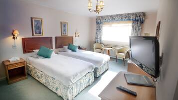 A hotel room with two beds, a TV, a desk, a chair, and a window with curtains.