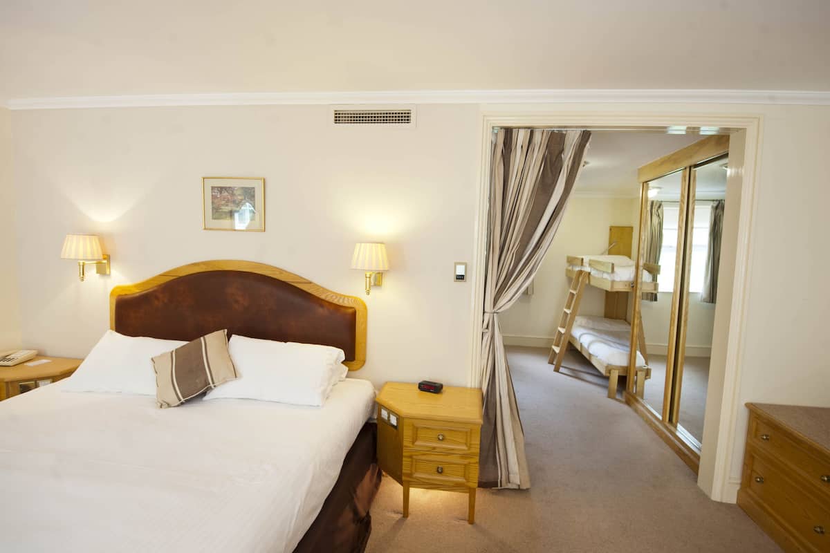 A hotel room with a large bed, bedside lamps, a nightstand, a wooden dresser, and a mirror.