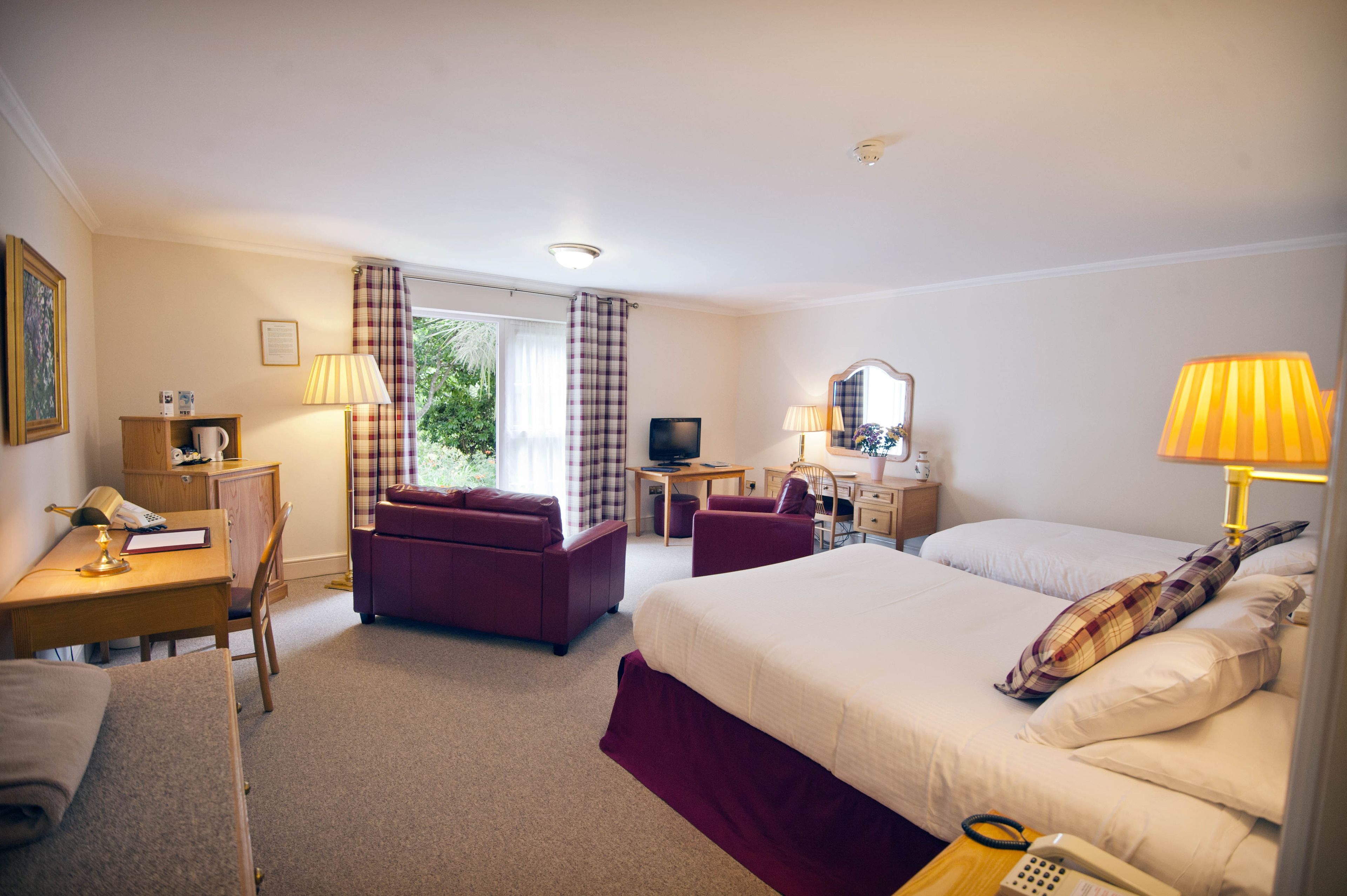 A hotel room with a bed, a desk, a chair, a sofa, a TV, and a window with curtains.