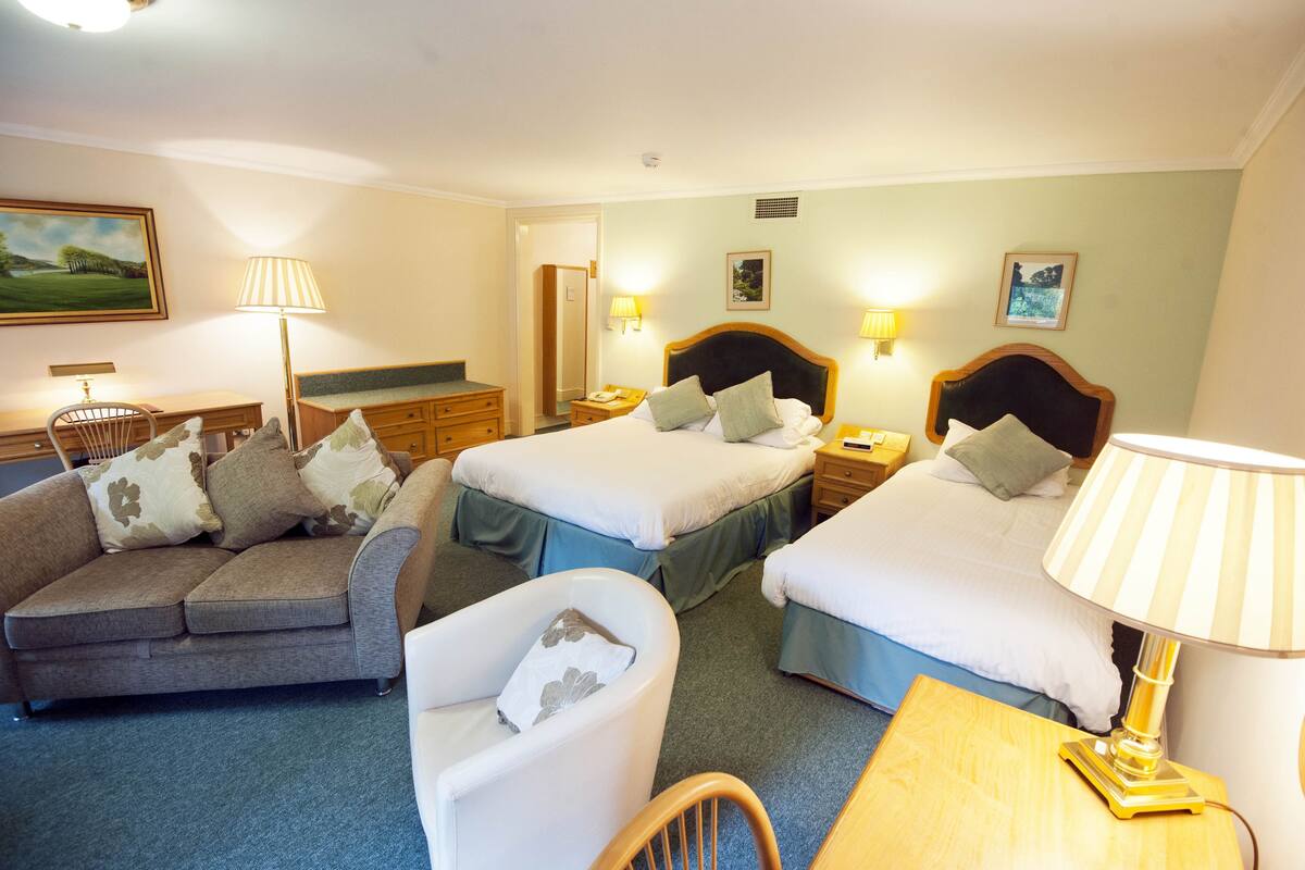 A hotel room with two beds, a sofa, a chair, a desk, and two bedside lamps.