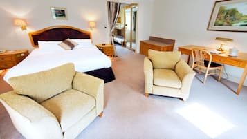 A hotel room with a large bed, two armchairs, a desk, and a chair.