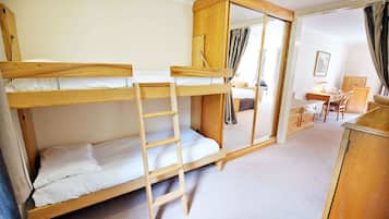 A bunk bed room with a ladder, wooden wardrobe, and a desk with a chair.