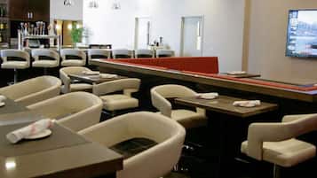 Een restaurant met een bar, tafels met servetten en een televisiescherm waarop een nieuwskanaal wordt vertoond.