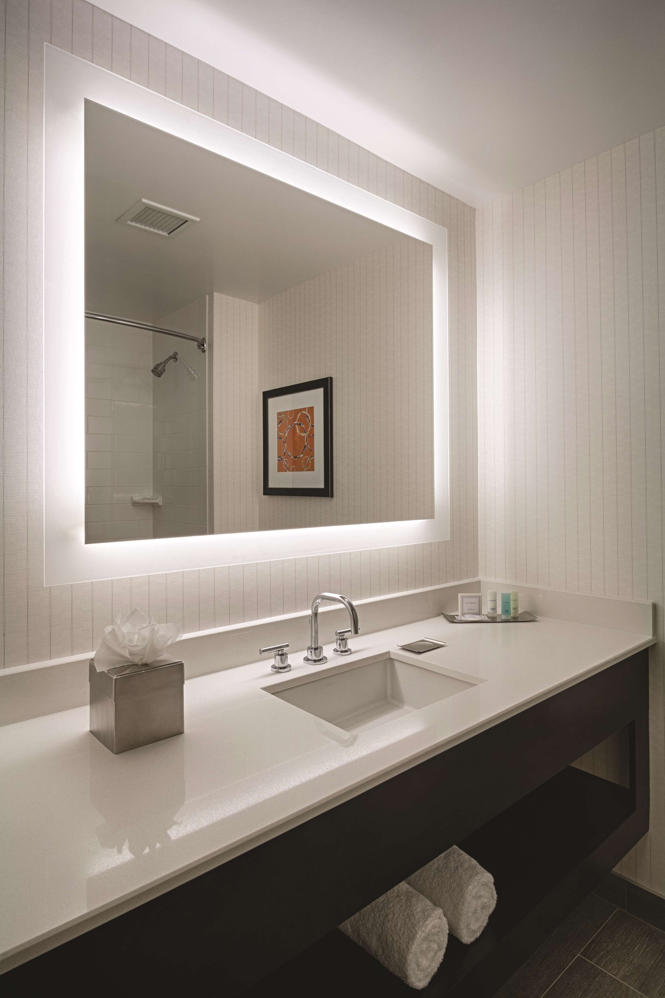 A modern bathroom with a large mirror, white sink, and dark vanity.