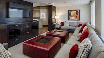 A modern living room with a sofa, two square ottomans, a flat-screen TV, and a kitchen in the background.