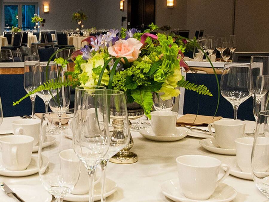 A dining area with round tables set for a formal meal, complete with white tablecloths, plates, cutlery, and wine glasses.