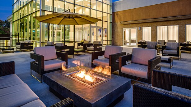 An outdoor seating area with fire pits and umbrellas, surrounded by modern buildings with large windows. - DoubleTree by Hilton Hotel Bristol, Connecticut (Bristol)