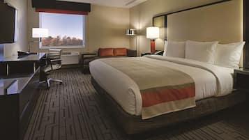 Een hotelkamer met een groot bed, een bureau, een stoel, een televisie en een raam met uitzicht op bomen.