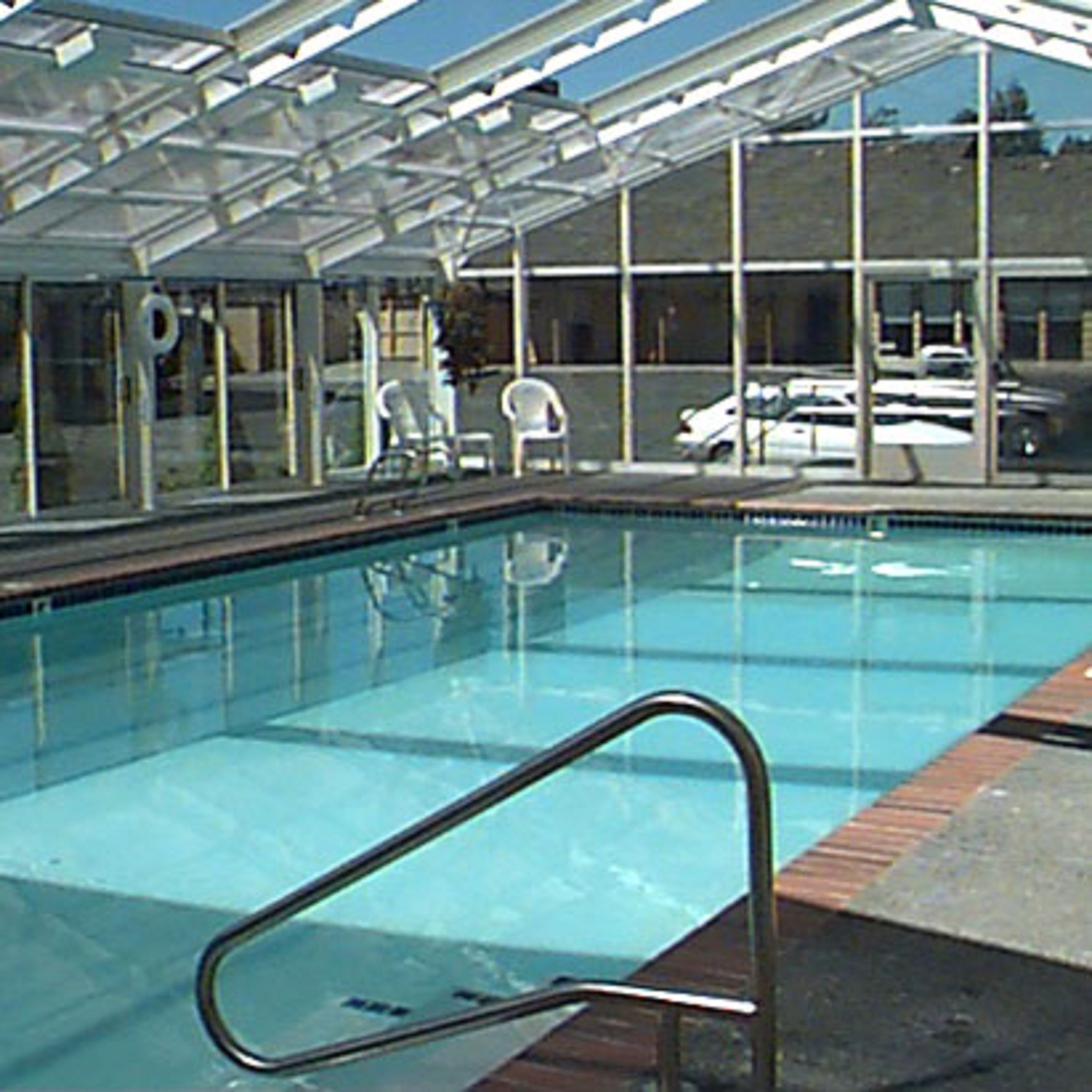 A swimming pool with a glass enclosure, clear water, and a metal pool ladder.