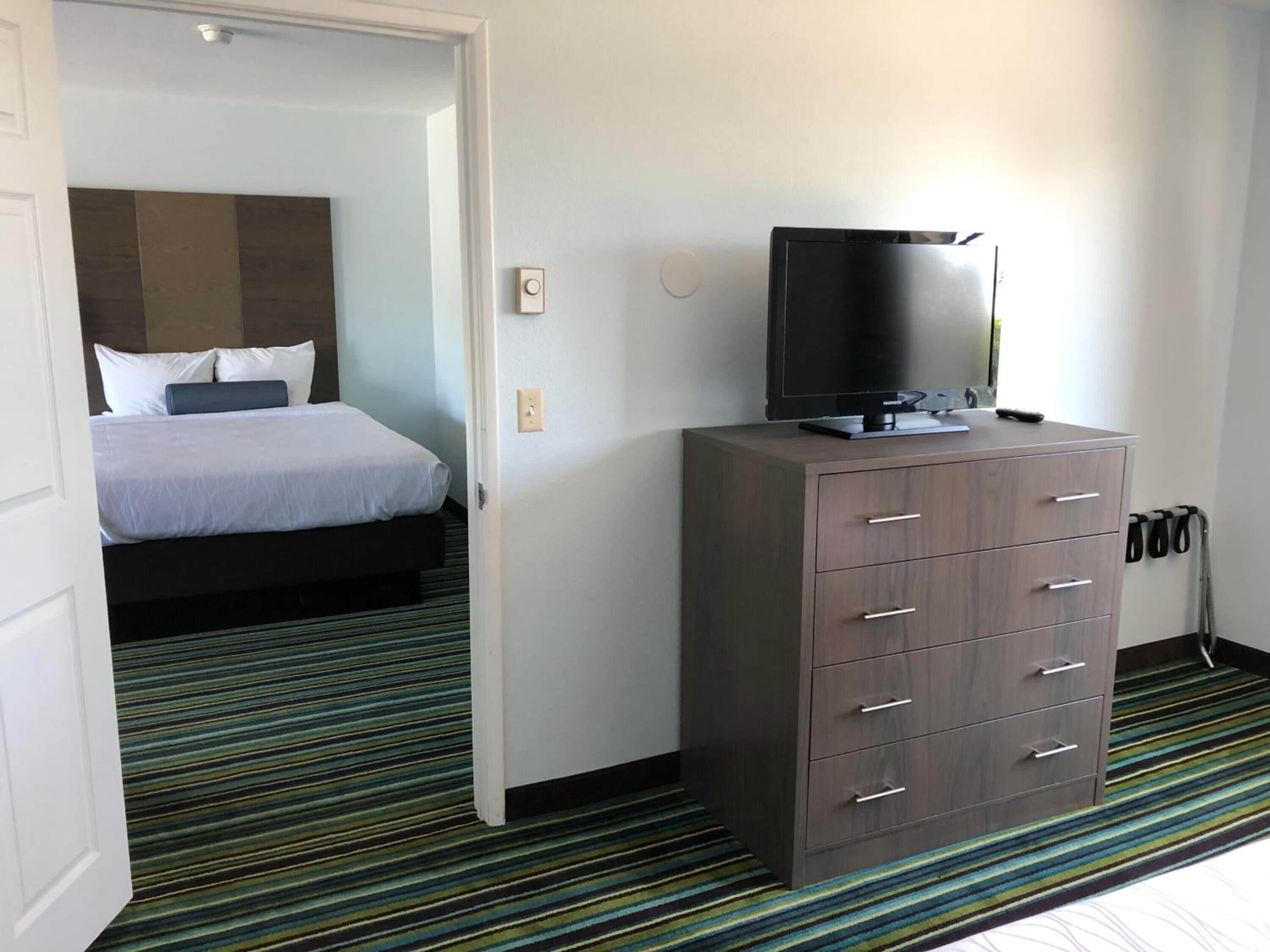 A hotel room with a bed, a TV on a dresser, and a striped carpet.