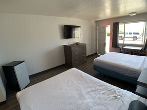 A hotel room with two beds, a TV mounted on the wall, a dresser, and a window with a view of parked cars outside.
