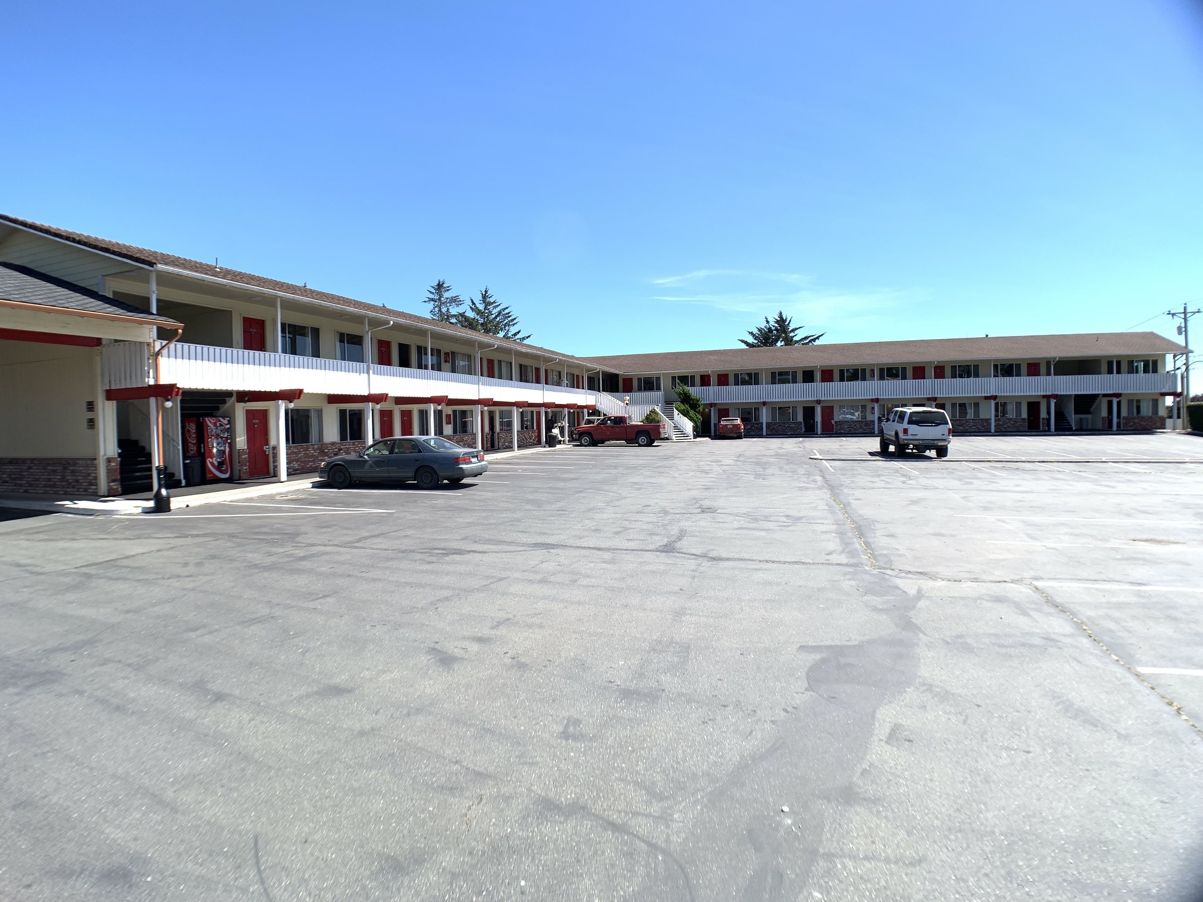 Ein Motel mit Parkplatz, mehreren Zimmern und blauem Himmel.