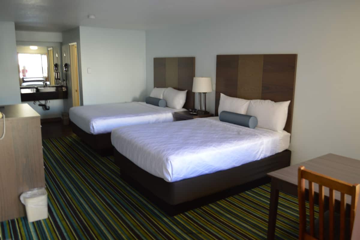Ein Hotelzimmer mit zwei Betten, einem Schreibtisch, einem Stuhl, einem Spiegel und einem durch eine offene Tür einsehbaren Badezimmer.