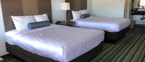 A hotel room with two beds, a nightstand, a lamp, and a bathroom visible through an open door.