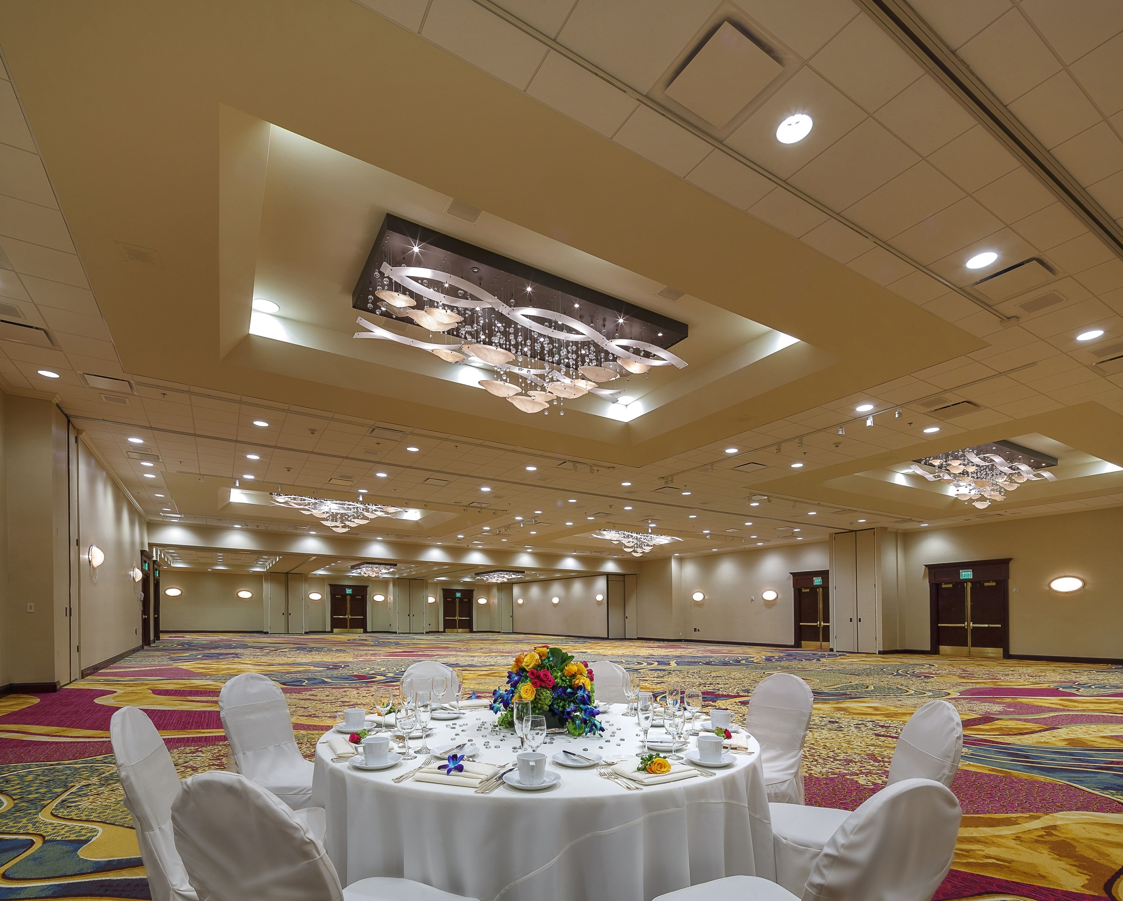 A banquet hall with round tables set for a formal event, featuring a chandelier and a large digital screen on the ceiling.