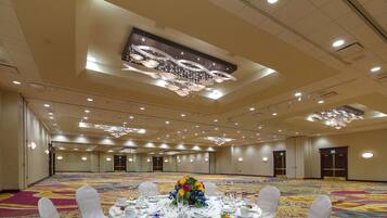 A banquet hall with round tables set for a formal event, featuring a chandelier and a large digital screen on the ceiling.