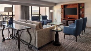 A hotel room with a sofa, two armchairs, a glass coffee table, a TV, and a balcony view. - Salt Lake Marriott Downtown at City Creek (Salt Lake City)