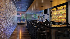 A modern bar area with a long counter, multiple stools, and a well-stocked liquor shelf. - Salt Lake Marriott Downtown at City Creek (Salt Lake City)