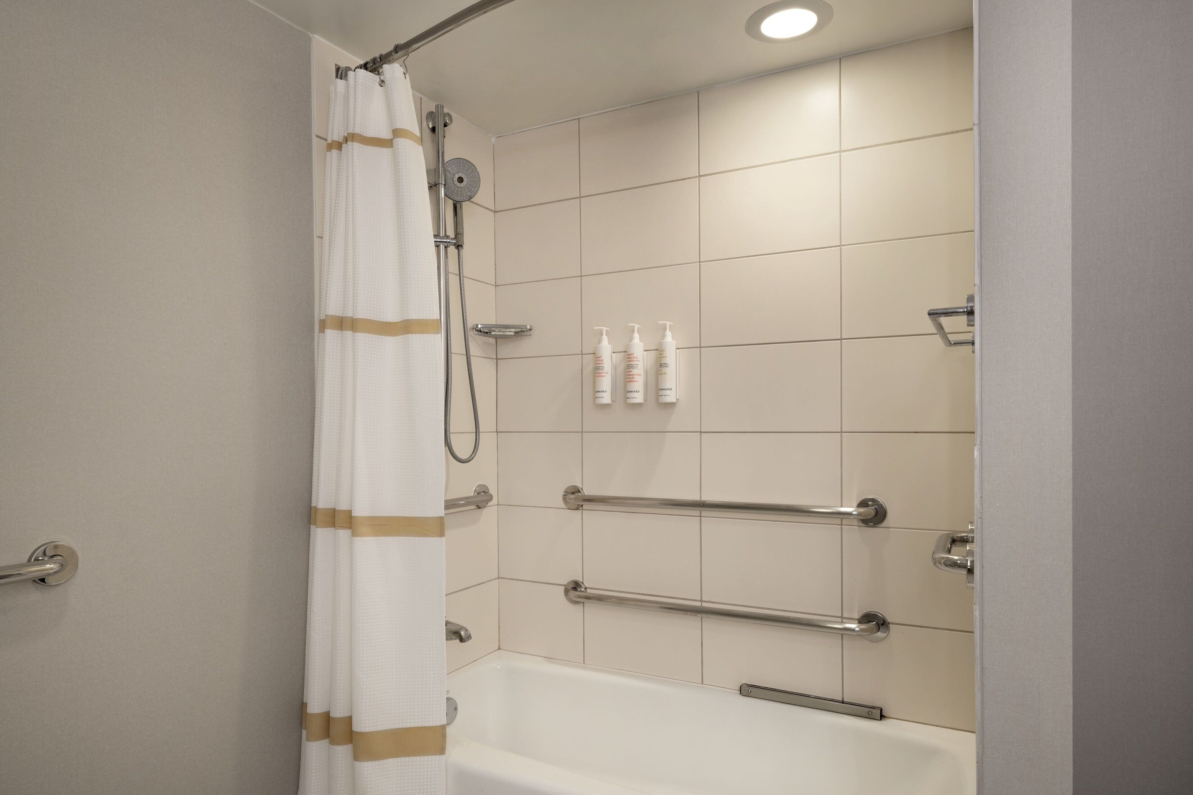 A bathroom with a bathtub, shower, and handrails.
